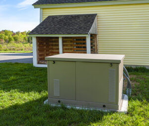 Residential standby generator installed on a concrete pad behind a yellow house