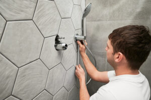 Male plumber installing a showerhead in a bathroom with hexagonal tile walls